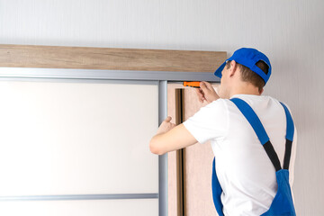 Wall Mural - Handyman who installs sliding doors at home in overalls with a screwdriver in his hands repairs the door