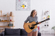 © LIGHTFIELD STUDIOS - happy mature woman with grey hair standing with acoustic guitar and laughing in living room