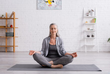 Mature Woman With Grey Hair Sitting In Lotus Pose On Yoga Mat