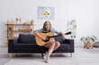 © LIGHTFIELD STUDIOS - cheerful mature woman with grey hair sitting on couch with acoustic guitar