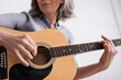 © LIGHTFIELD STUDIOS - cropped view of middle aged woman playing acoustic guitar in living room