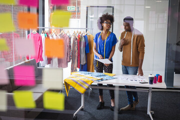 Diverse male and female fashion designers at work discussing and looking at sketches