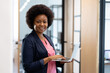 © WavebreakMediaMicro - Happy african american businesswoman standing in corridor using laptop looking to camera