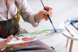 © LIGHTFIELD STUDIOS - cropped view of middle aged woman holding paintbrush and palette with colorful paints