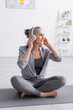© LIGHTFIELD STUDIOS - happy middle aged woman in wireless headphones sitting in lotus pose on yoga mat at home