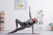 © LIGHTFIELD STUDIOS - flexible middle aged woman in sportwear with raised hand practicing yoga on mat at home