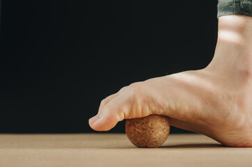 Artistic isolated close up foot on cork massage ball on cork yoga mat for plantar fascia massage and hydration on black background with copy space. Concept: self care practices at home