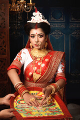 Wall Mural - Portrait of beautiful Indian woman wearing traditional saree and gold jewellery, tossing a handful of rice over her head. Bengali Hindu marriage.