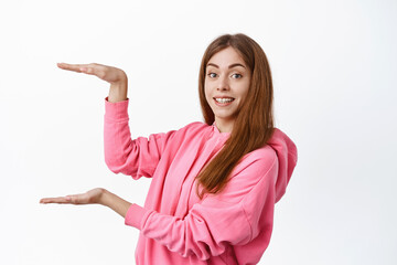 Wall Mural - Cheerful young woman showing big large size on copyspace, display product or logo, holding empty space for banner, standing over white background