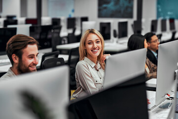Working at a computer. Young adult business people work at computers with colleagues in a spacious office. Data analysis, statistics, finance. Training, business team, programming, development.