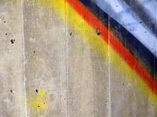 Yellow, Red, Blue, White And Black Sprayed In Diagonal Stripes On A Grey Concrete Wall