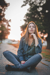 Poster - Young Caucasian female wearing a shirt and ripped jeans sitting on the road