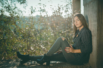 Sticker - Young Caucasian female wearing a shirt and ripped jeans sitting on a concrete wall