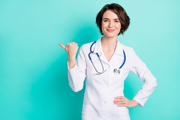 Wall Mural - Photo of young woman doctor happy smile indicate thumb empty space advice ad choice suggest isolated over teal color background