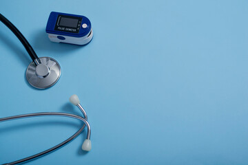 Flat composition with pulse oximeter and stethoscope on blue background.A pulse oximeter used to measure heart rate and oxygen levels.