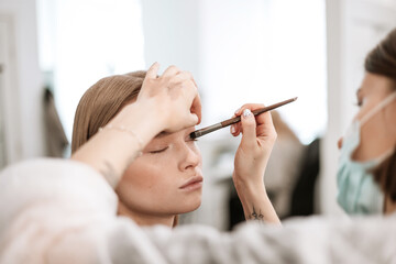 Sticker - makeup artist applies eye shadow to the eyelids on a beautiful young woman blonde model, face make up concept