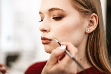 Wall Mural - makeup artist paints lips with lipstick with a brush on a beautiful young woman blonde model, face make up concept