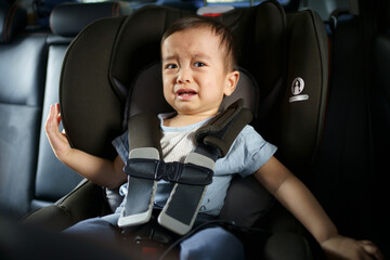 Asian little baby crying and sad while fastened belt and seat in the safety car seat. A boy looking his mother and unhappy in a car.