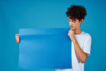 Cheerful guy with curly hair and blue mockup poster advertising