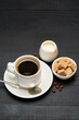 Cup of espresso coffee and pot of cream or milk on dark wooden background