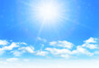 Sunny day background, blue sky with white cumulus clouds and glaring sun