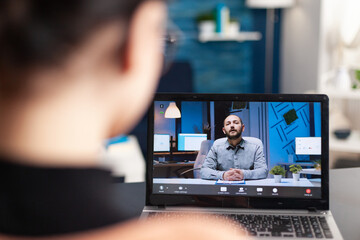 Student discussing with her teacher on online videocall about e-learning platform using laptop computer. Young woman having remote education during coronavirus quarantine while sitting in living room