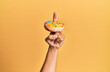 Finger of hispanic man holding donut over isolated yellow background.
