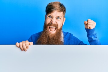 Sticker - Young irish redhead man holding blank empty banner screaming proud, celebrating victory and success very excited with raised arm