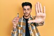 © Krakenimages.com - Young hispanic man holding electronic cigarette with open hand doing stop sign with serious and confident expression, defense gesture