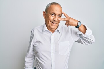 Wall Mural - Handsome senior man wearing casual white shirt doing peace symbol with fingers over face, smiling cheerful showing victory