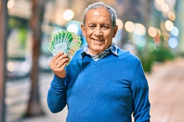 Wall Mural - senior grey-haired man smiling happy holding russian ruble banknotes at the city.