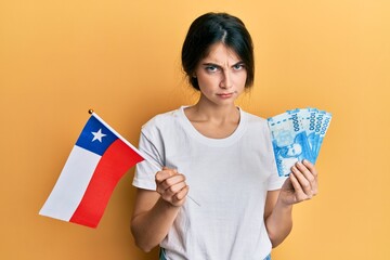 Poster - Young caucasian woman holding chile flag and chilean pesos banknotes skeptic and nervous, frowning upset because of problem. negative person.