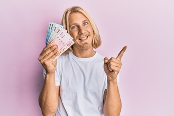 Sticker - Caucasian young man with long hair holding new taiwan dollars banknotes smiling happy pointing with hand and finger to the side