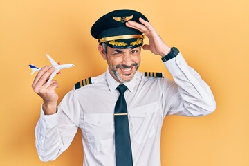 Sticker - Handsome middle age man with grey hair wearing airplane pilot uniform holding toy plane stressed and frustrated with hand on head, surprised and angry face