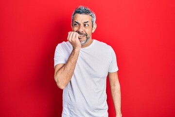 Sticker - Handsome middle age man with grey hair wearing casual white t shirt looking stressed and nervous with hands on mouth biting nails. anxiety problem.