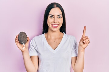 Poster - Beautiful woman with blue eyes holding pumice stone smiling with an idea or question pointing finger with happy face, number one