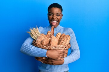 Sticker - Young african american woman holding wicker basket with bread celebrating crazy and amazed for success with open eyes screaming excited.