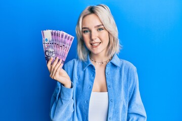 Poster - Young blonde girl holding philippine peso banknotes looking positive and happy standing and smiling with a confident smile showing teeth