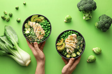 Female hands and bowls of tasty salad with fresh vegetables and chicken on color background