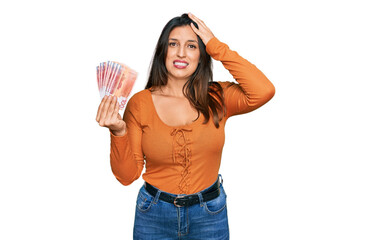 Wall Mural - Beautiful hispanic woman holding norwegian krone banknotes stressed and frustrated with hand on head, surprised and angry face