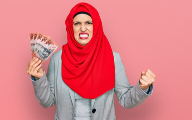 Sticker - Beautiful hispanic woman wearing islamic hijab holding australian dollars banknotes annoyed and frustrated shouting with anger, yelling crazy with anger and hand raised