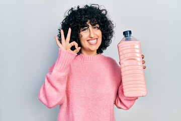 Sticker - Young middle east woman holding detergent bottle doing ok sign with fingers, smiling friendly gesturing excellent symbol