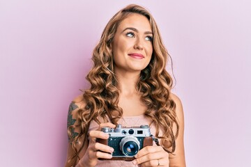 Poster - Young blonde girl holding vintage camera smiling looking to the side and staring away thinking.