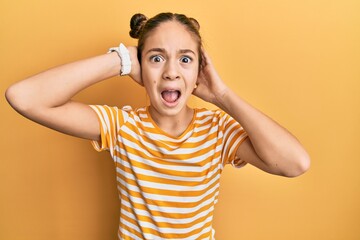 Beautiful brunette little girl wearing casual striped t shirt crazy and scared with hands on head, afraid and surprised of shock with open mouth