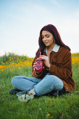 Wall Mural - Teenager girl drinking water in a red jar sitting on the grass of a hill. She has a salad next to her.