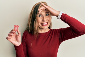 Poster - Young blonde woman holding menstrual cup stressed and frustrated with hand on head, surprised and angry face