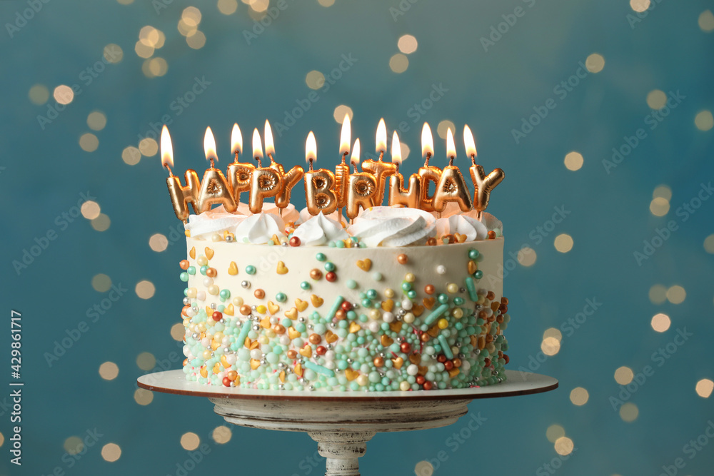 Beautiful birthday cake with burning candles on stand against festive ...