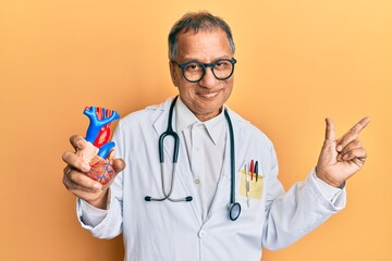 Wall Mural - Middle age indian man wearing doctor uniform holding heart smiling happy pointing with hand and finger to the side