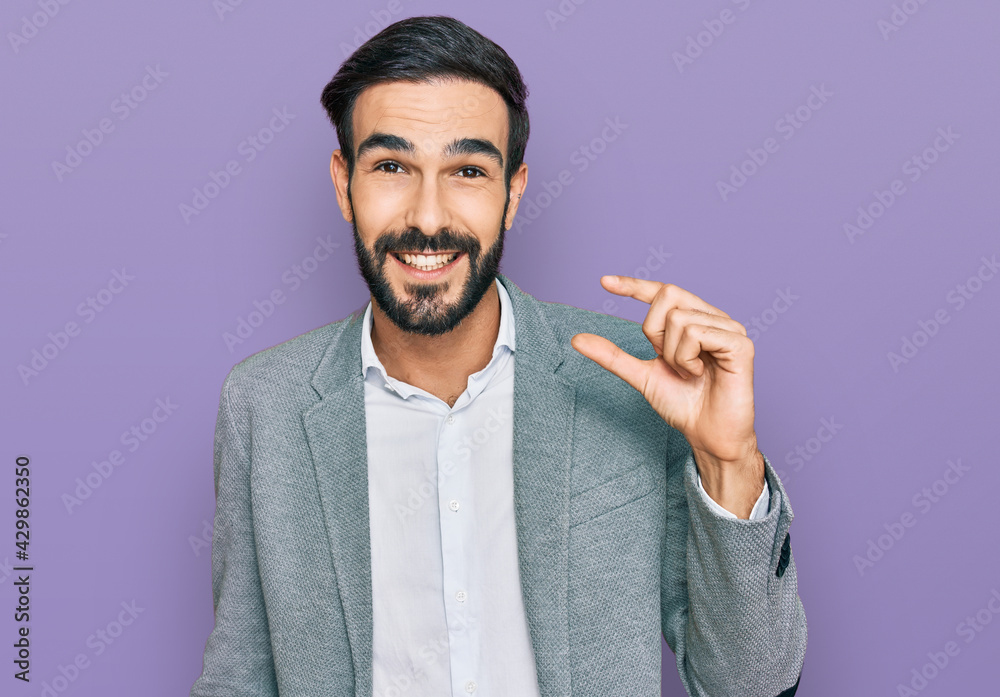 Young hispanic man wearing business clothes smiling and confident gesturing with hand doing small size sign with fingers looking and the camera. measure concept. - obrazy, fototapety, plakaty 
