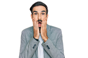 Wall Mural - Young hispanic man wearing business clothes afraid and shocked, surprise and amazed expression with hands on face